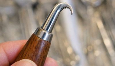 Small metal tool with a hooked, serrated end and a wooden handle. Found it mixed in with old silverware. Too sharp to be a spoon, too curved for a knife.